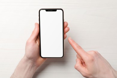 Photo of Man holding smartphone with blank screen at white wooden table, top view. Mockup for design