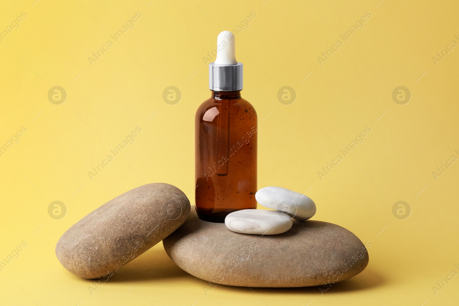 Photo of Bottle of face serum and spa stones on yellow background