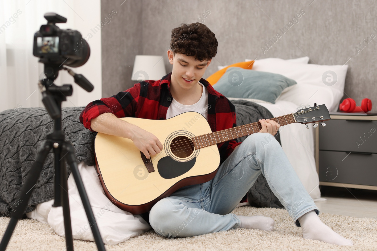 Photo of Smiling teenage blogger playing guitar while streaming at home