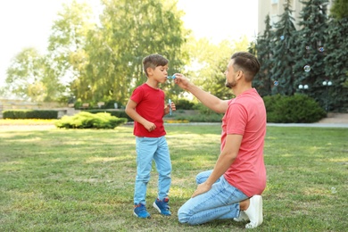 Photo of Father and his cute child playing with soap bubbles in green park on sunny day. Happy family