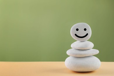 Photo of Stack of stones with drawn happy face on beige table against light green background, space for text. Zen concept