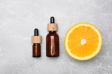 Photo of Bottles of essential oil with orange slice on grey table, flat lay