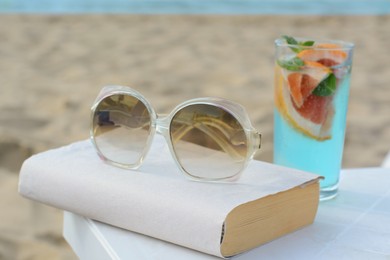 Photo of Book, sunglasses and glass of refreshing drink on beach
