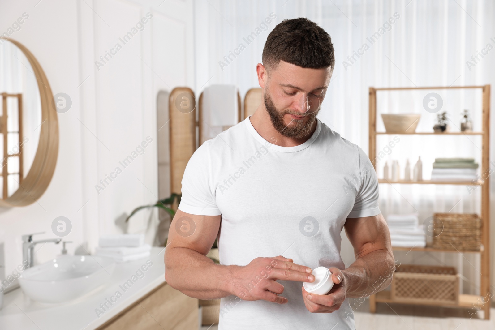 Photo of Handsome man applying body cream in bathroom