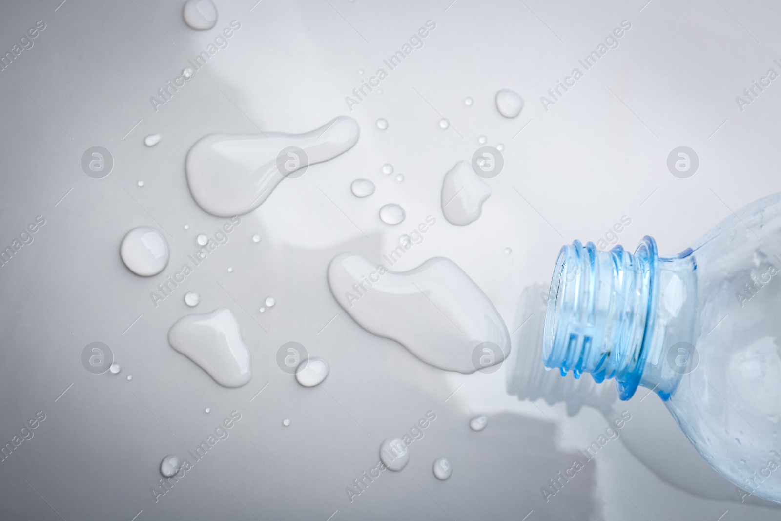 Photo of Drops of spilled water and plastic bottle on grey background, top view