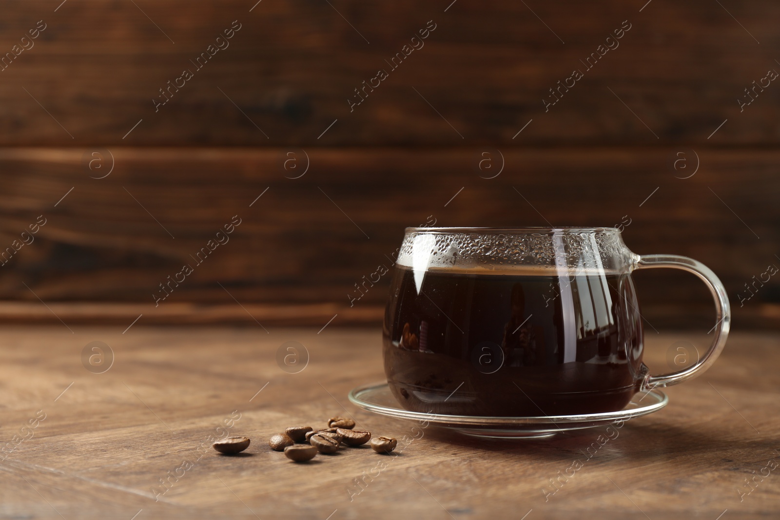 Photo of Hot coffee in glass cup and beans on wooden table, closeup. Space for text