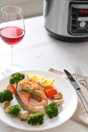 Photo of Plate with salmon steak and garnish prepared in multi cooker on table