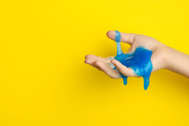 Photo of Woman playing with blue slime on yellow background, closeup. Antistress toy