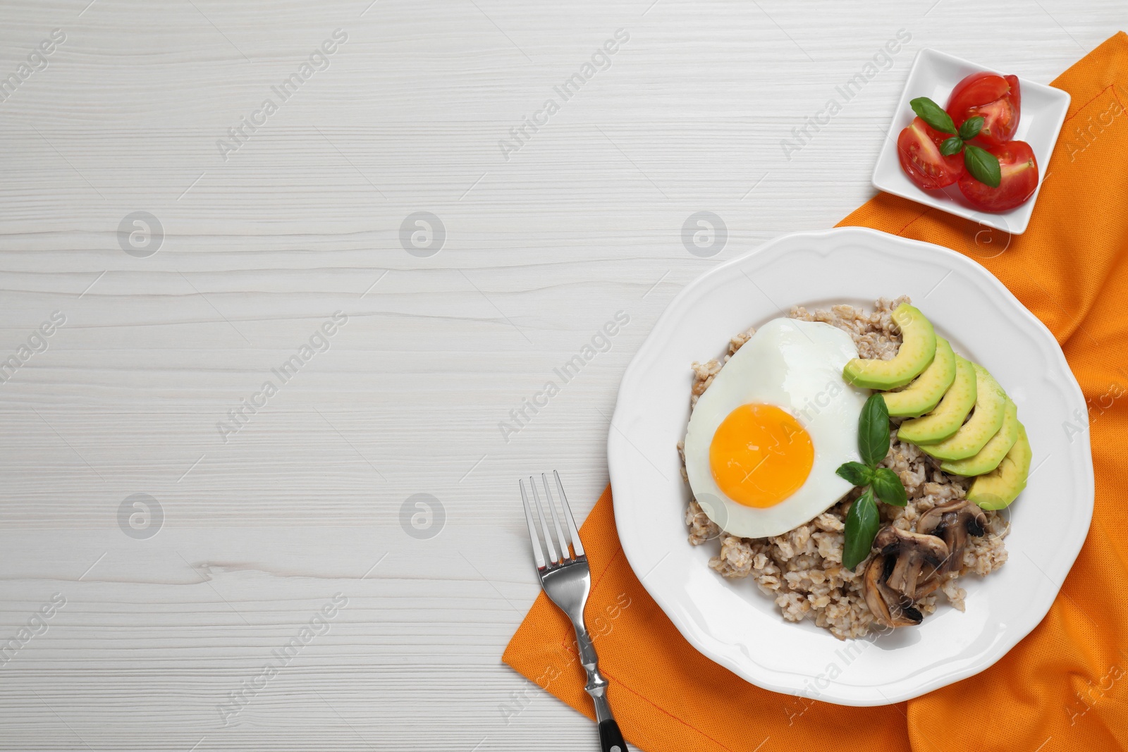 Photo of Tasty boiled oatmeal with fried egg, avocado and mushrooms served on white wooden table, flat lay . Space for text