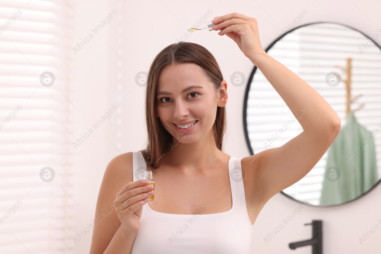 Photo of Beautiful woman applying serum onto hair indoors