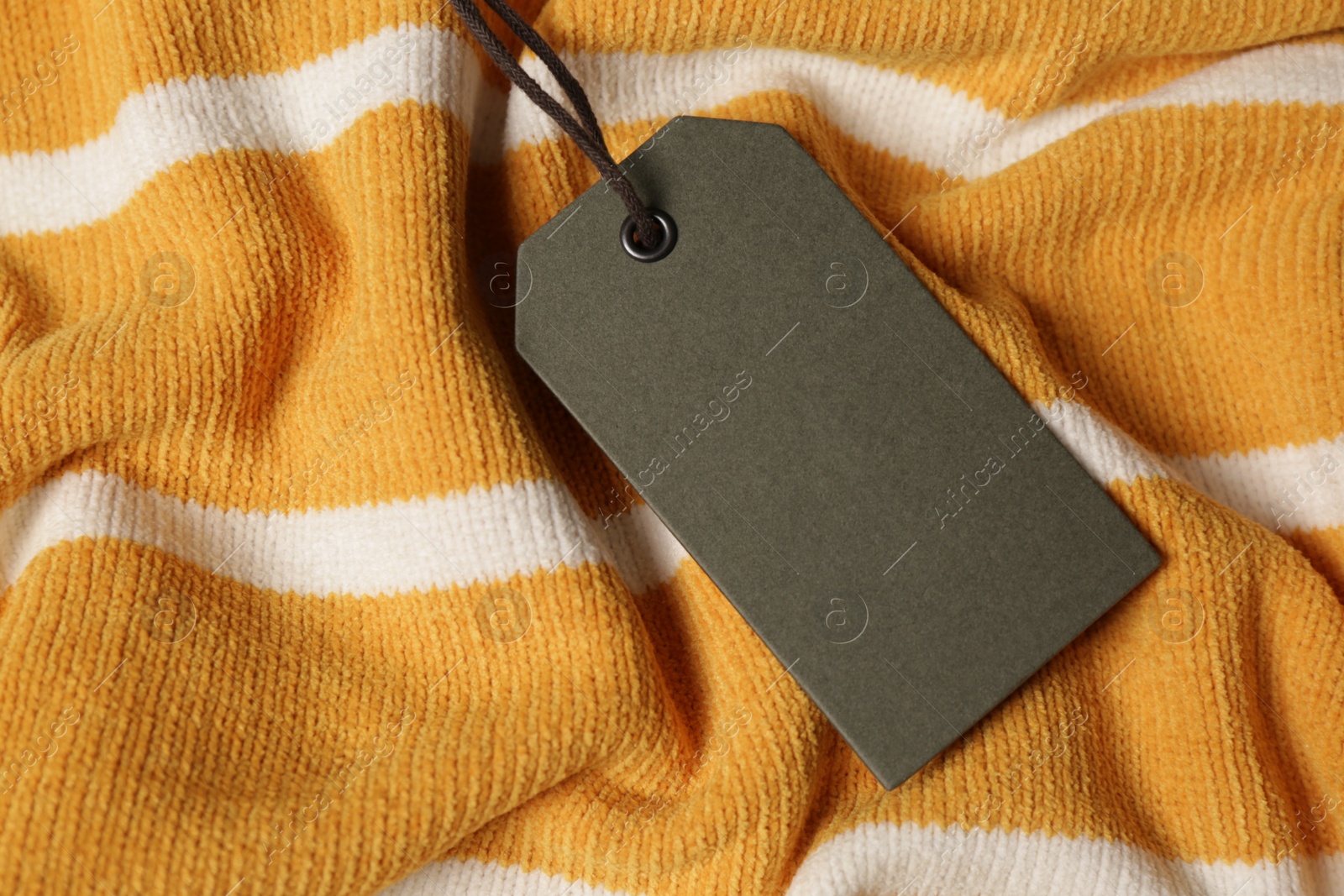 Photo of Blank grey tag on striped sweater, top view. Space for text