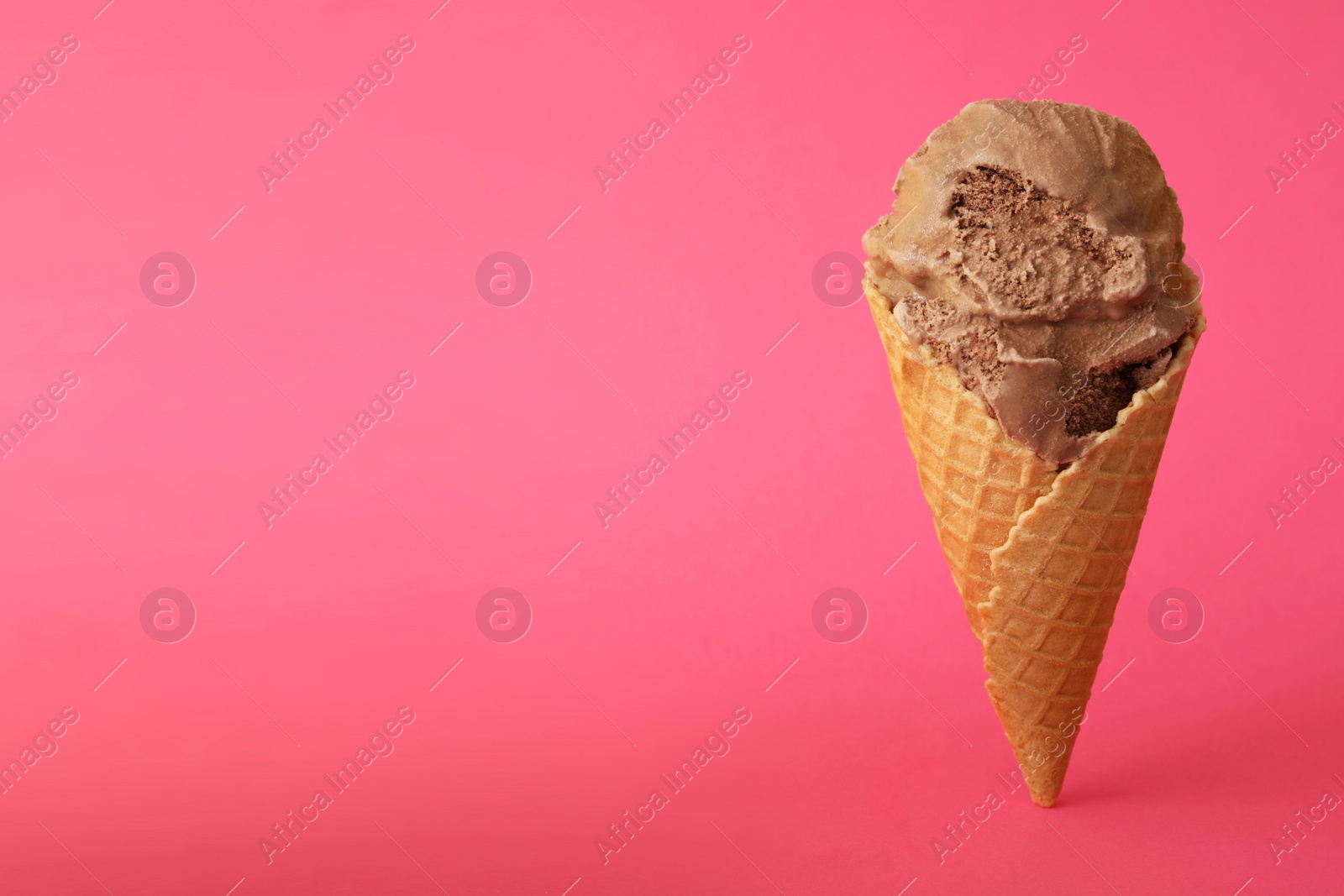 Photo of Delicious chocolate ice cream in waffle cone on pink background. Space for text