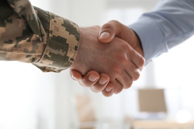 Soldier and businessman shaking hands indoors, closeup