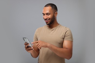 Photo of Happy man sending message via smartphone on grey background