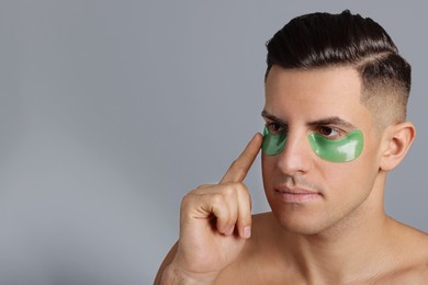 Photo of Man applying green under eye patch on grey background. Space for text