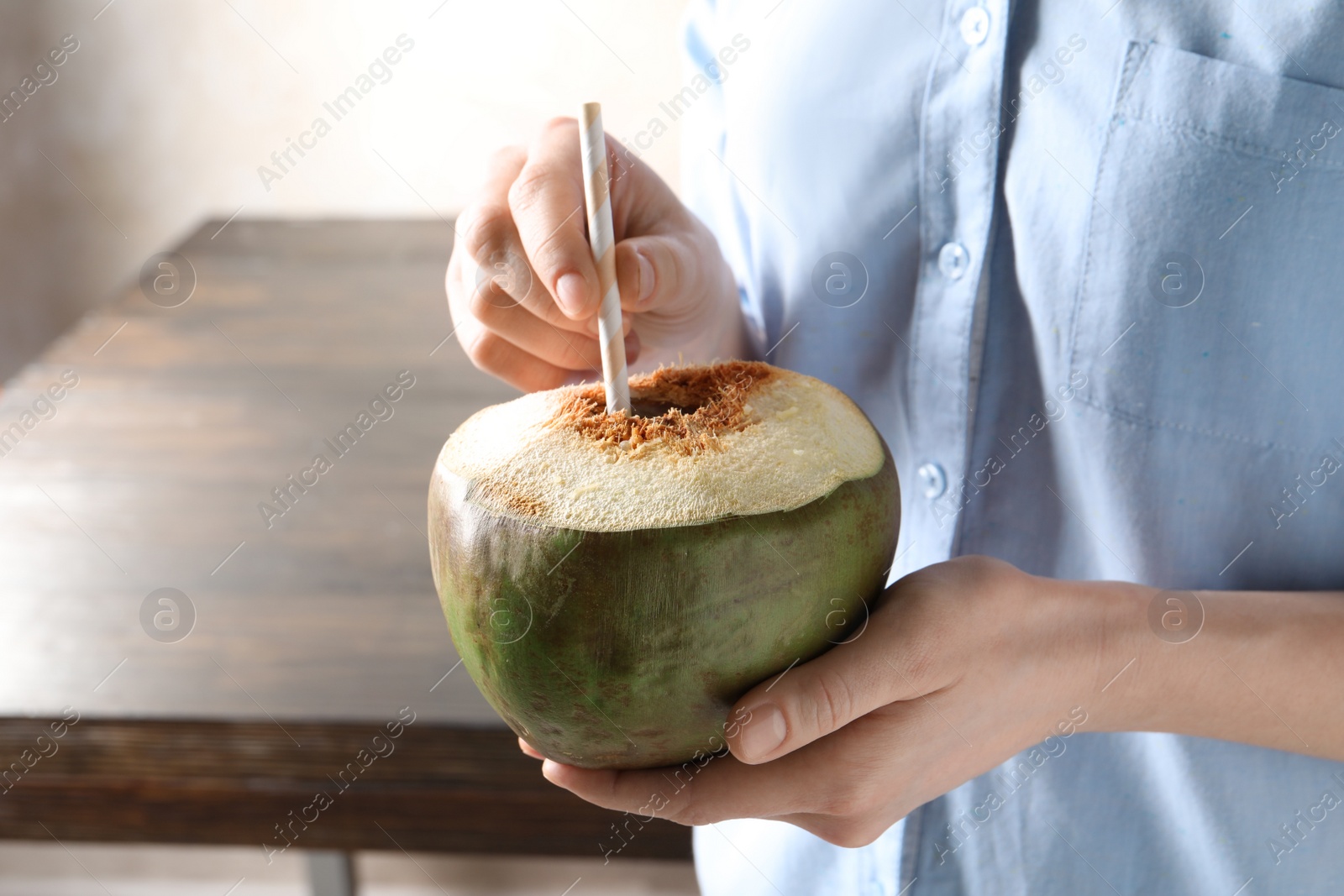 Photo of Young woman with fresh coconut cocktail on blurred background, closeup