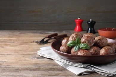 Photo of Tasty cooked meatballs with basil served on wooden table. Space for text