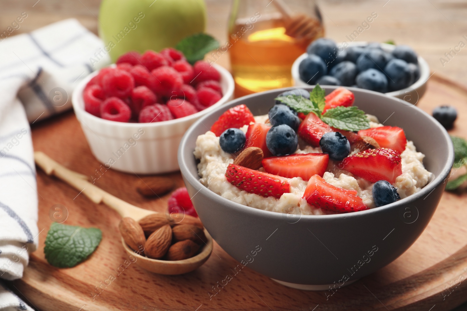 Photo of Tasty oatmeal porridge with berries and almond nuts in bowl served on wooden board