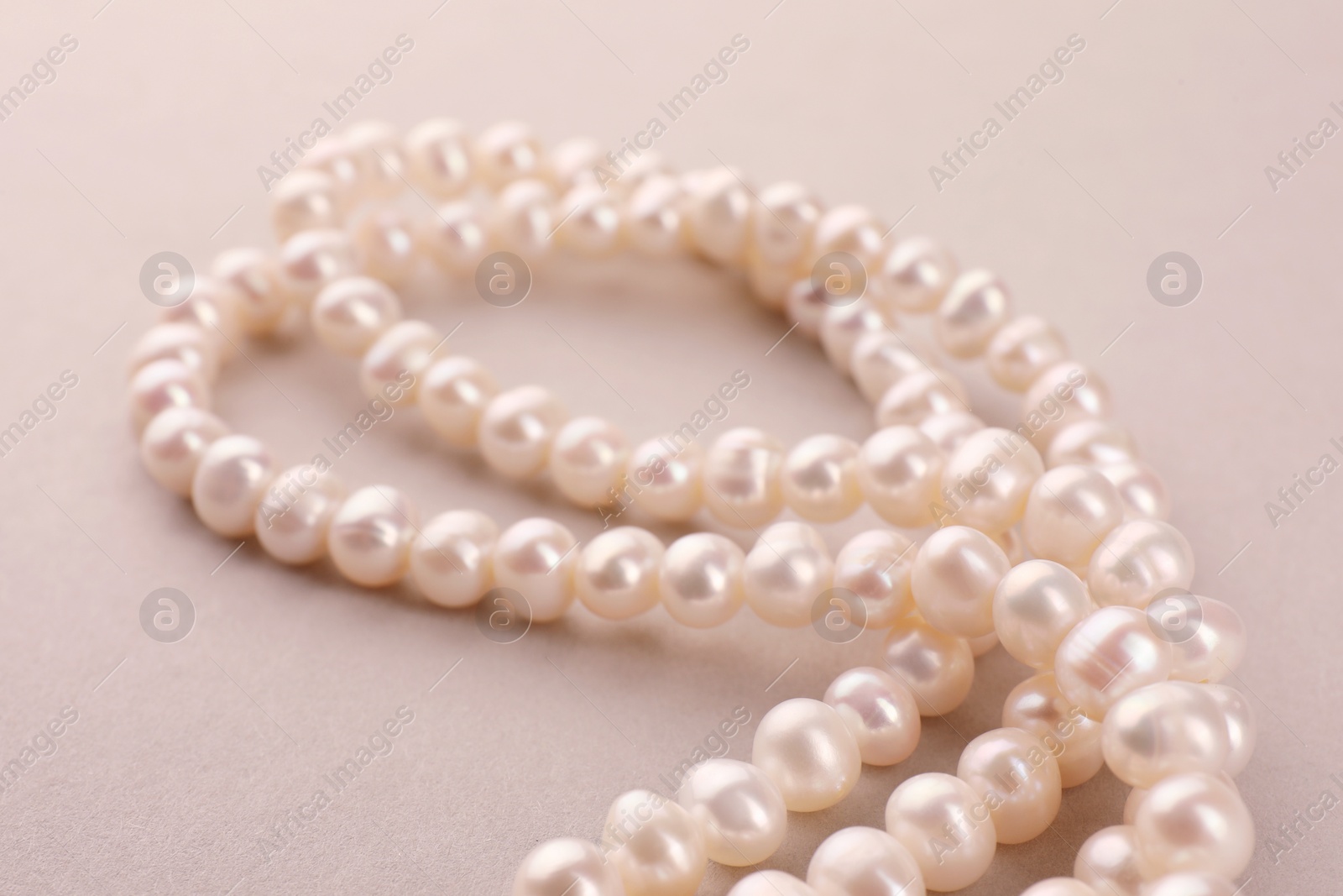 Photo of Elegant pearl necklace on beige background, closeup