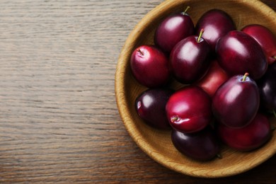 Photo of Bowl with tasty ripe plums on wooden table, top view. Space for text
