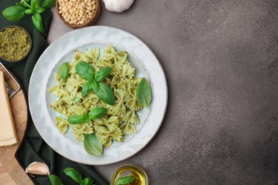 Photo of Delicious pasta with pesto sauce and ingredients on dark textured table, flat lay. Space for text