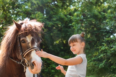 Photo of Cute little girl with her pony in green park