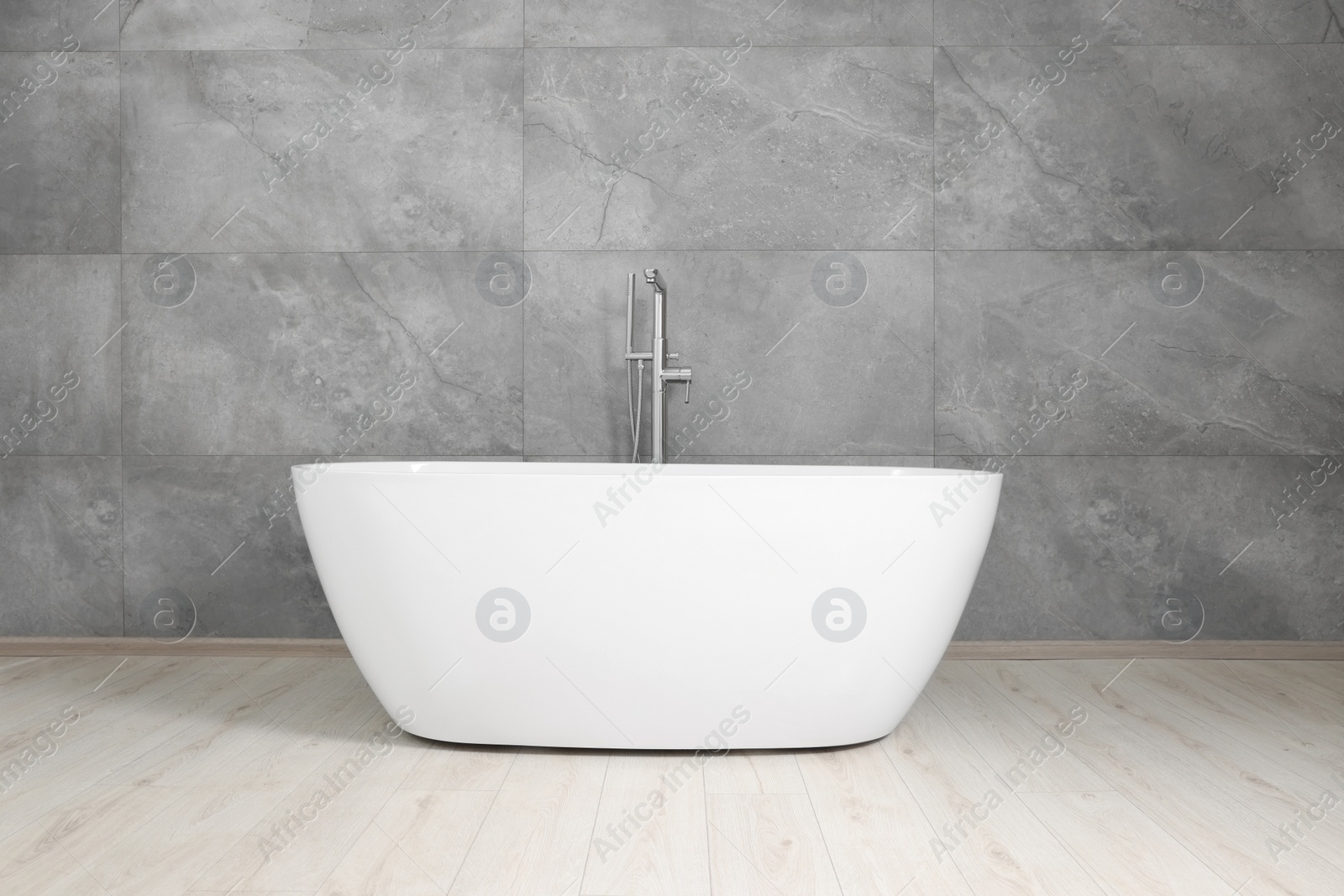 Photo of Stylish ceramic tub near light grey tiled wall indoors