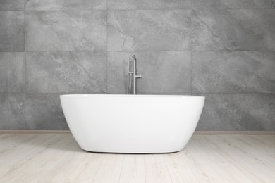 Stylish ceramic tub near light grey tiled wall indoors