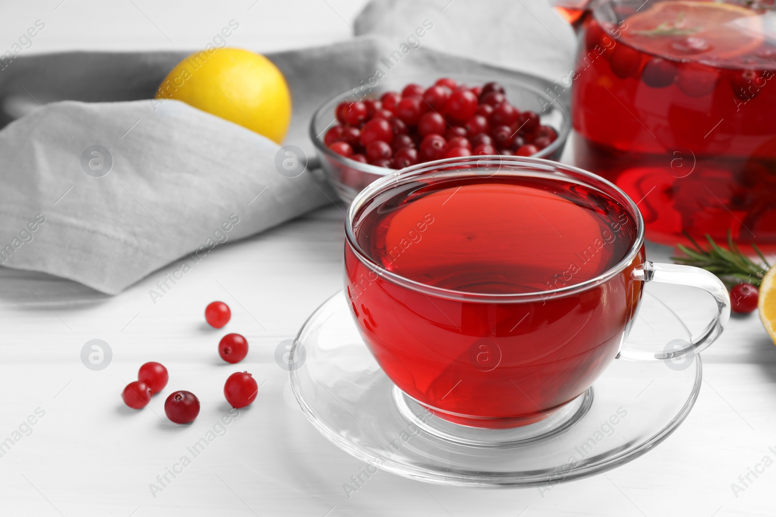 Photo of Tasty hot cranberry tea in glass cup and fresh berries on white table