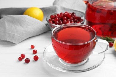 Photo of Tasty hot cranberry tea in glass cup and fresh berries on white table