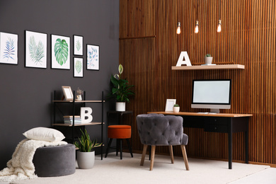 Photo of Comfortable workplace with computer near wooden wall in stylish room interior. Home office design
