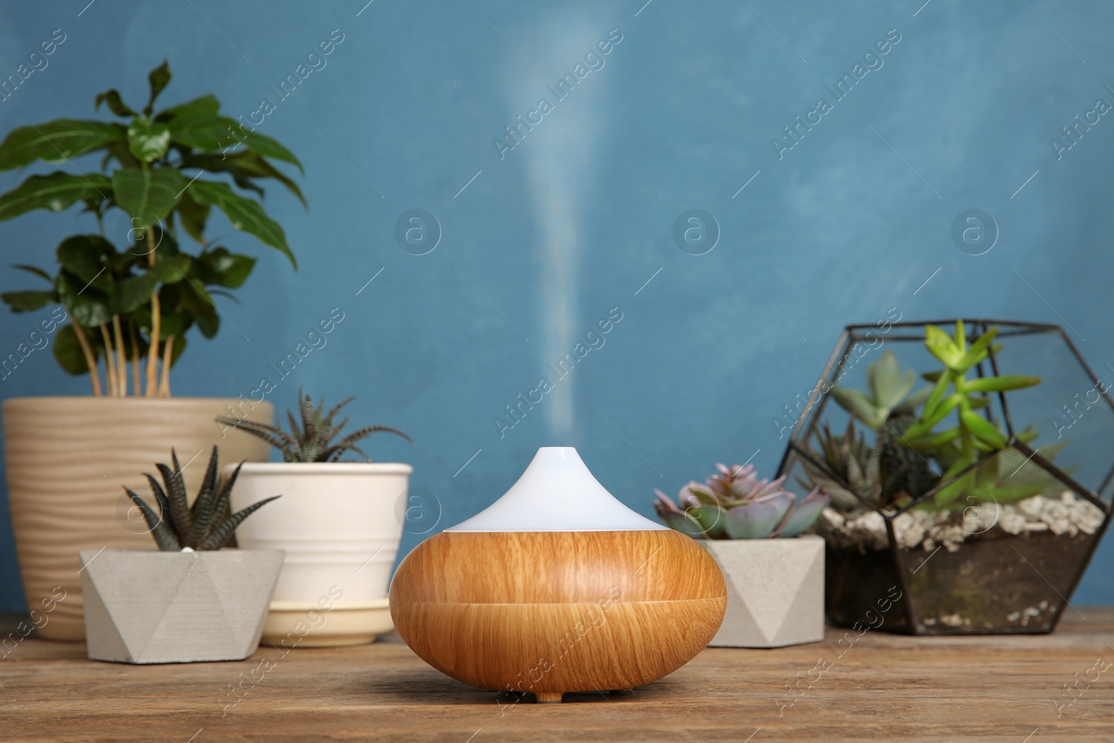 Photo of Composition with modern essential oil diffuser on wooden table against blue background, space for text