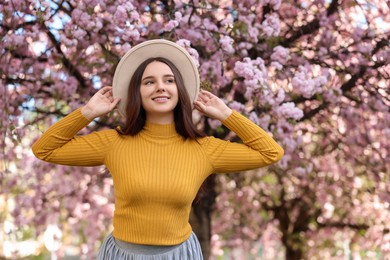 Beautiful woman in hat near blossoming tree on spring day