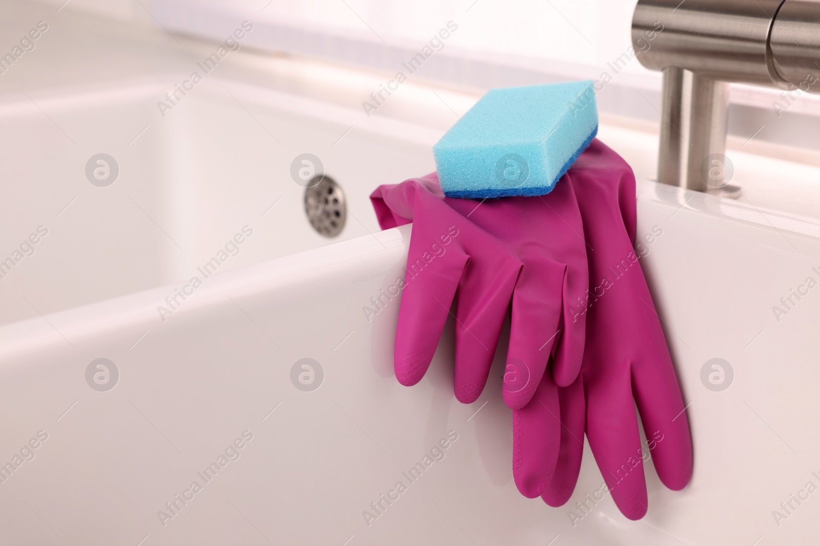 Photo of Sponge and rubber gloves on kitchen sink indoors