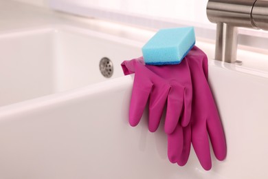 Photo of Sponge and rubber gloves on kitchen sink indoors