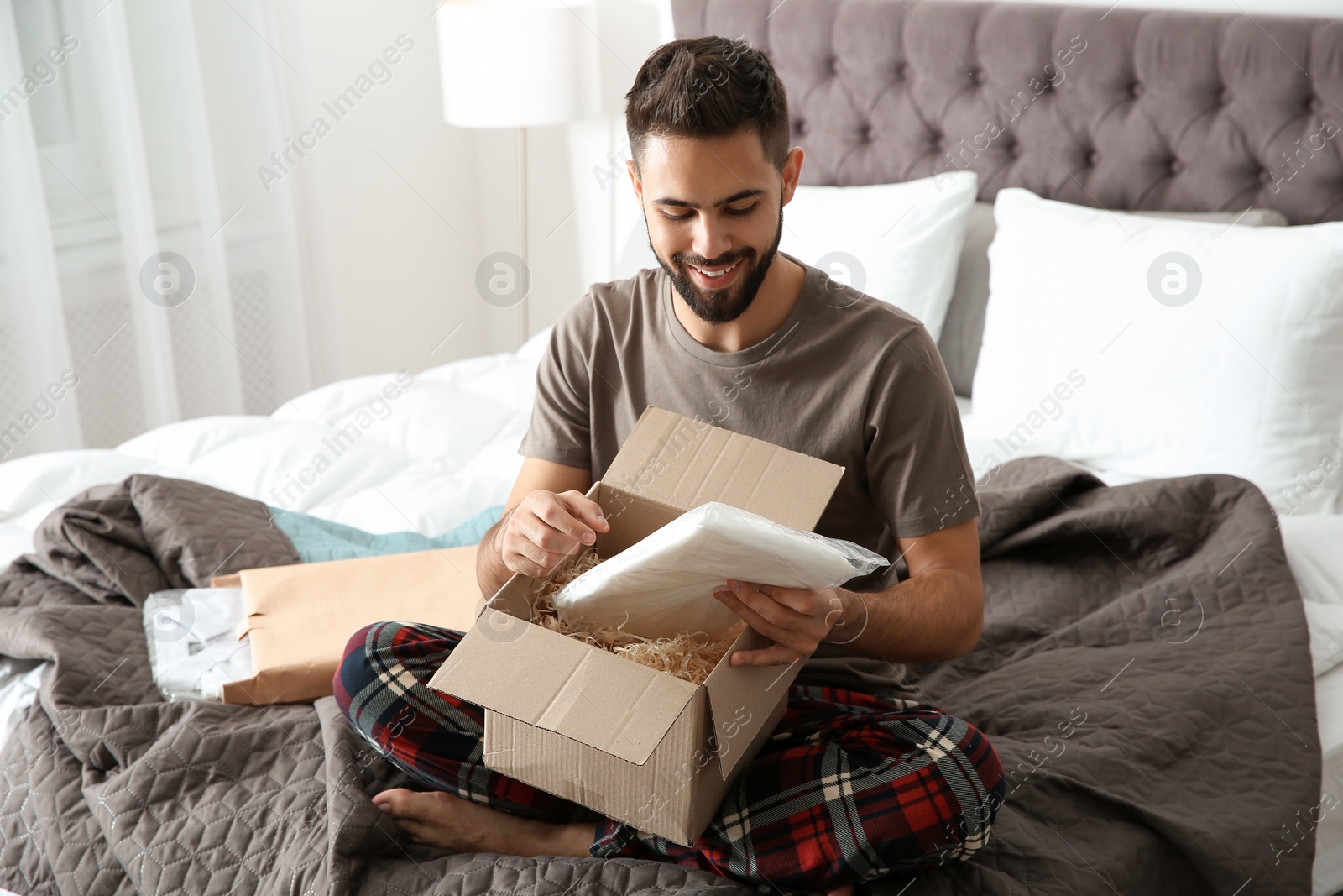 Photo of Young man opening parcel in bedroom at home