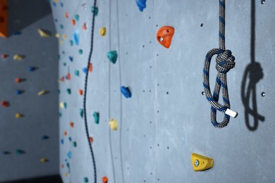 Photo of Climbing rope and colorful wall with holds in gym, space for text
