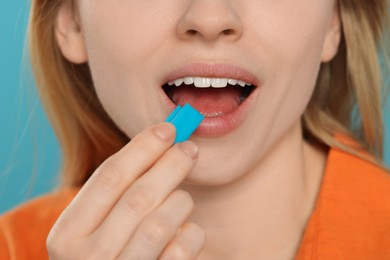 Woman putting bubble gum into mouth on light blue background, closeup