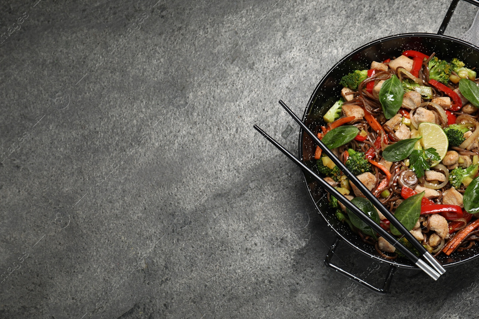 Photo of Stir-fry. Tasty noodles with meat in wok and chopsticks on grey textured table, top view. Space for text