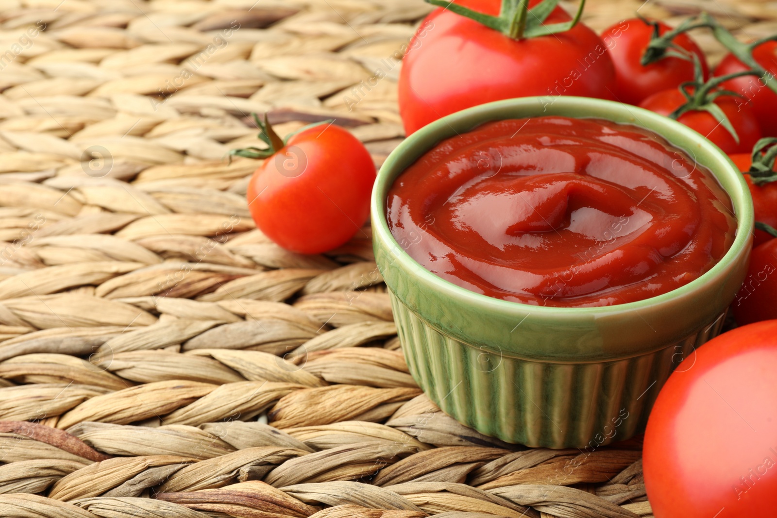 Photo of Bowl of tasty ketchup and tomatoes on wicker mat, closeup. Space for text