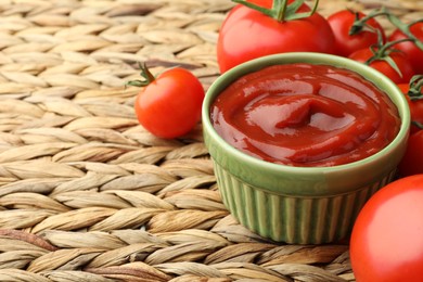Photo of Bowl of tasty ketchup and tomatoes on wicker mat, closeup. Space for text