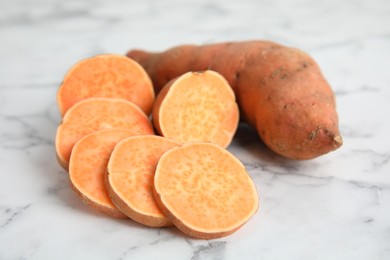 Photo of Whole and cut ripe sweet potatoes on white marble table, closeup