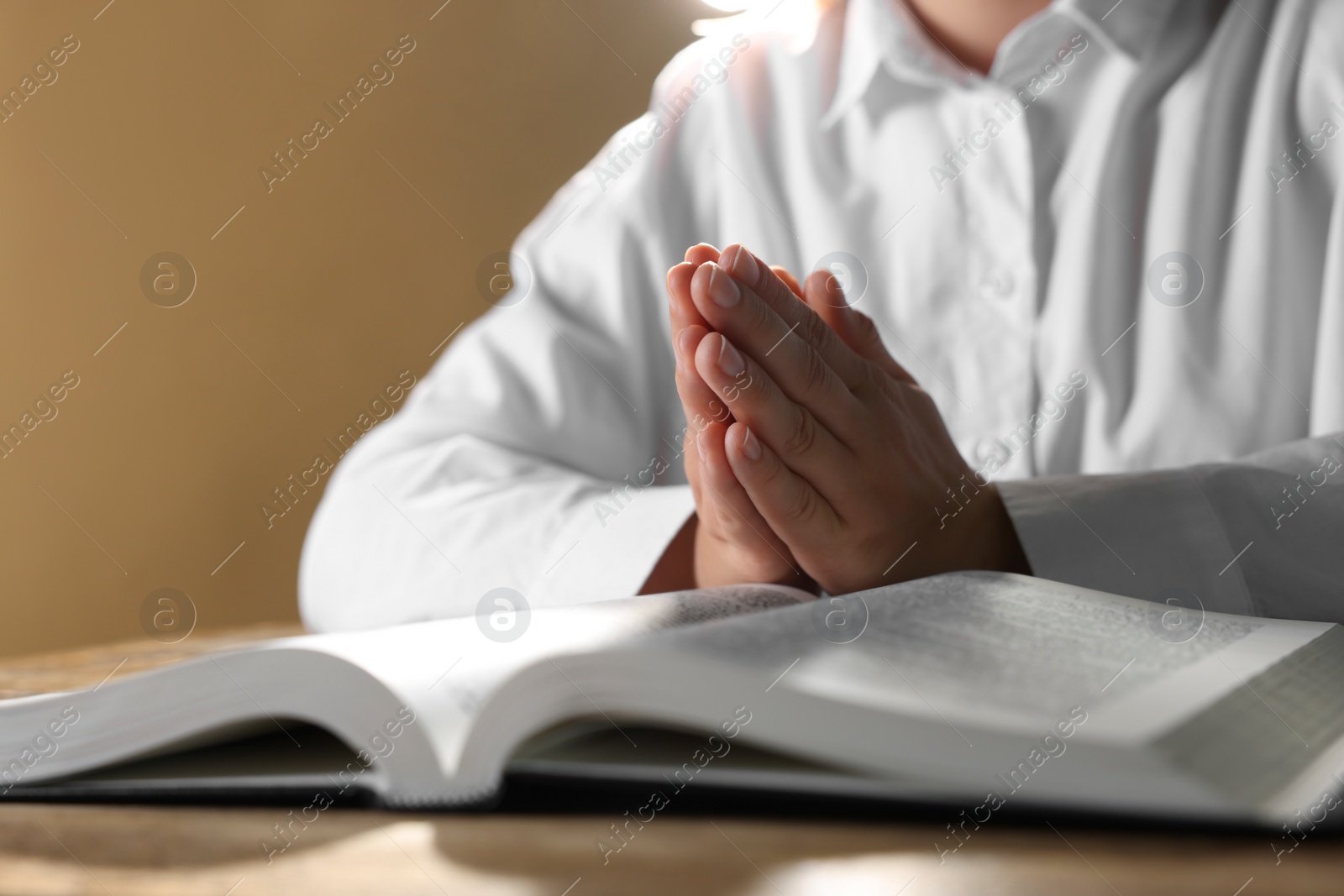 Photo of Woman holding hands clasped while praying over Bible at wooden table, closeup