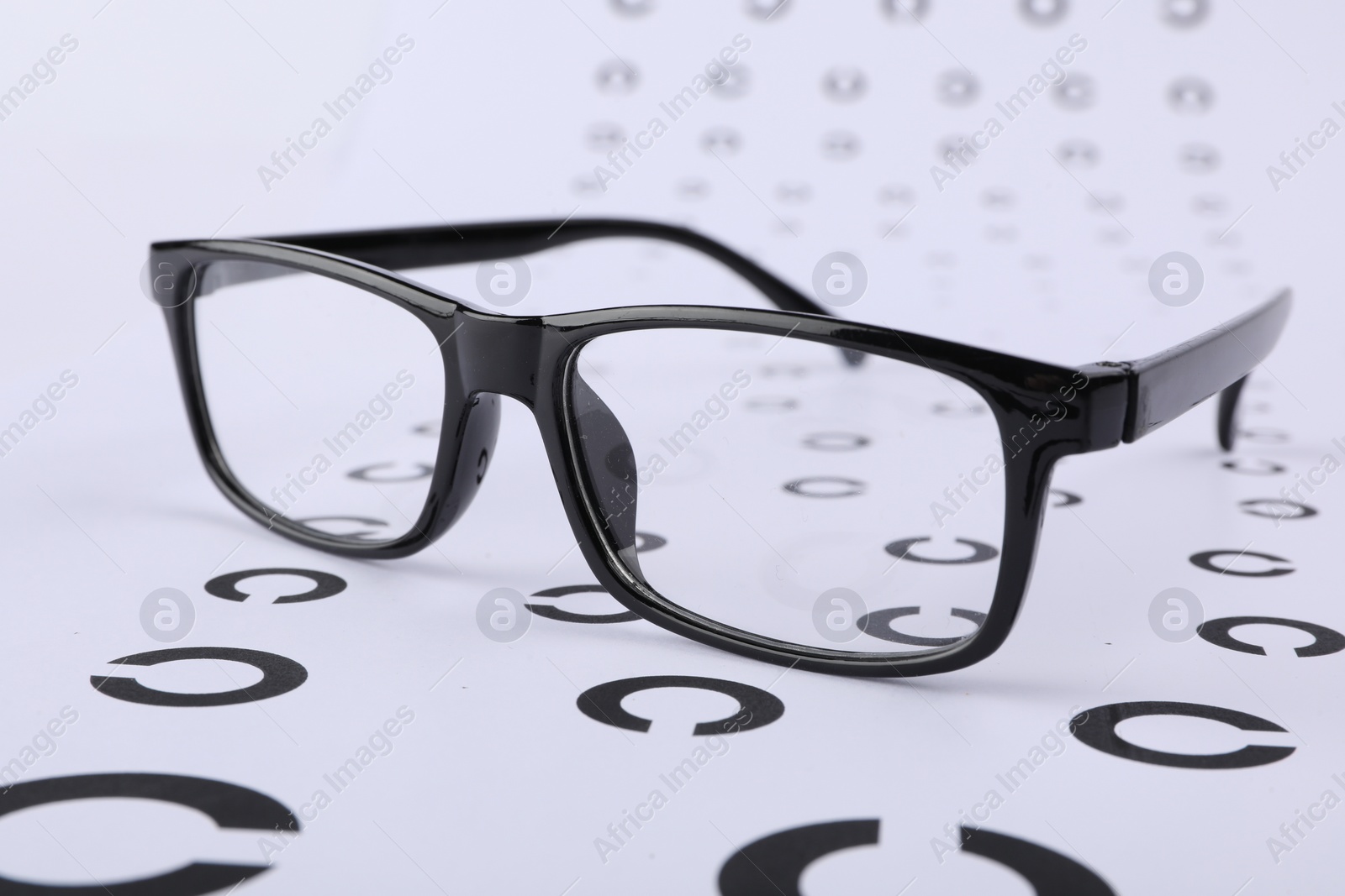 Photo of Vision test chart and glasses on white background, closeup