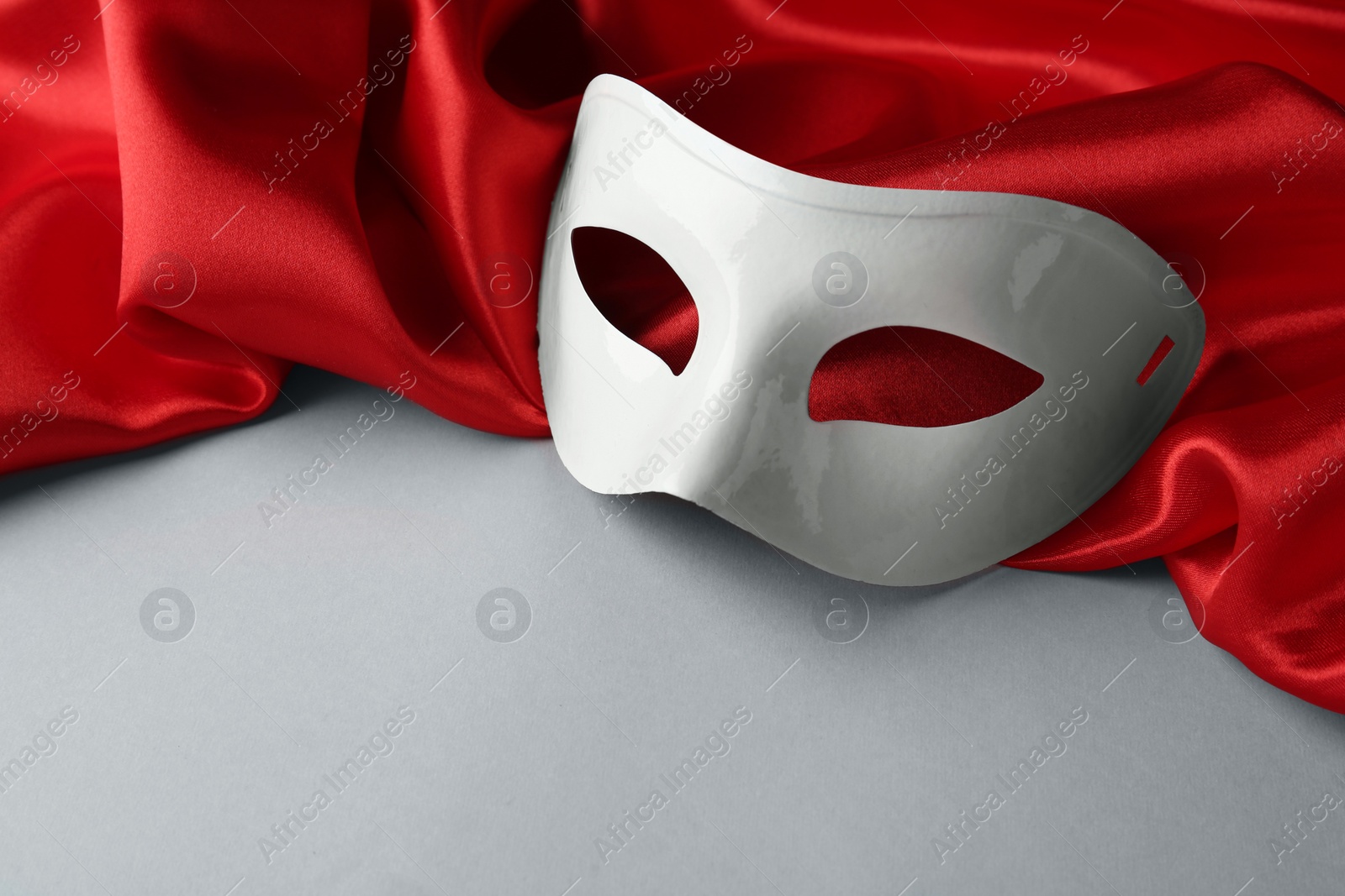 Photo of White theatre mask and red fabric on grey background, space for text