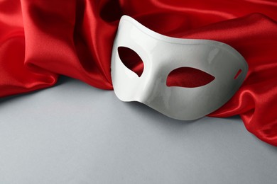 White theatre mask and red fabric on grey background, space for text