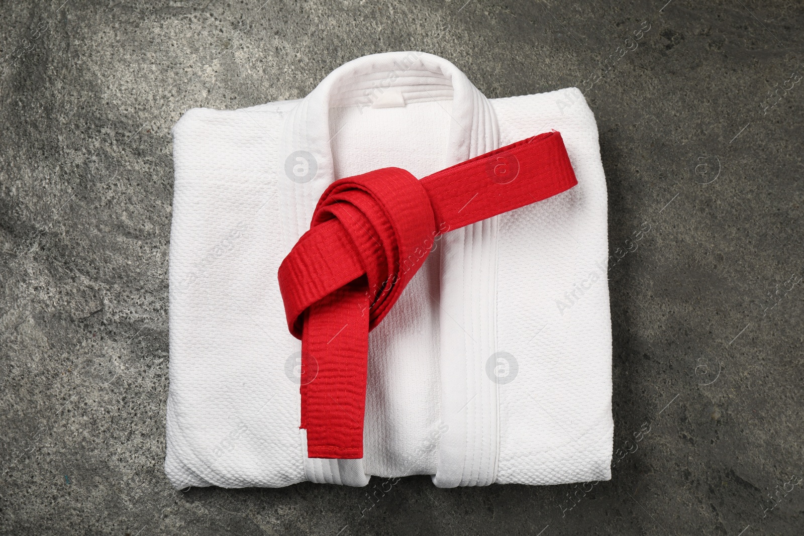 Photo of Red karate belt and white kimono on gray textured background, top view