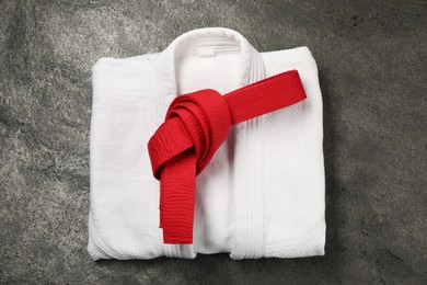 Red karate belt and white kimono on gray textured background, top view