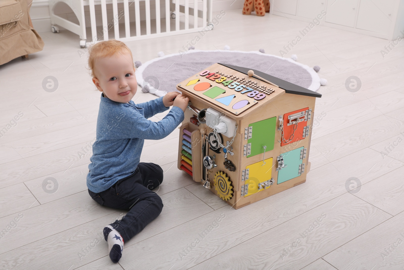 Photo of Cute little boy playing with busy board house on floor at home