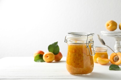Jar of apricot jam and fresh fruits on white wooden table. Space for text